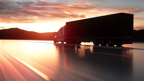 A Big Rig driving down the road at sunset.