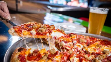 Lifting a slice from a meat lovers pizza.